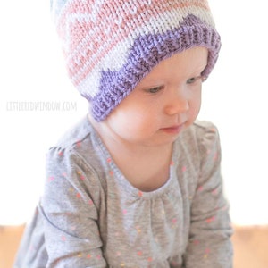 little girl wearing pink purple and blue easter egg patterned knit hat and looking off down and to the right