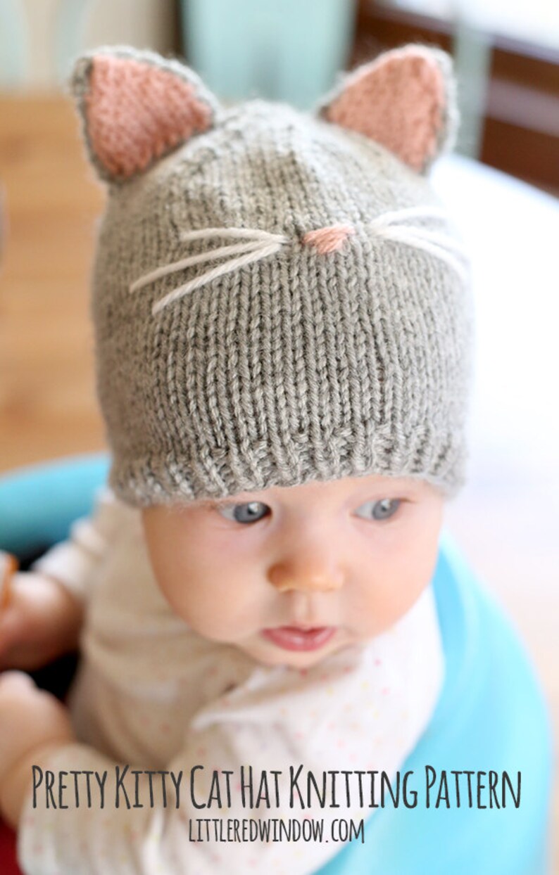 view from above of baby in gray onesie wearing a gray knit hat with pink cat ears on top and a little pink nose and white whiskers on the front, looking off into the distance while sitting a blue bumbo chair