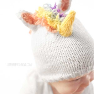 View of knit unicorn hat from slightly above on a baby showing rainbow loop stitch mane, pink and white unicorn ears and yellow knit unicorn horn