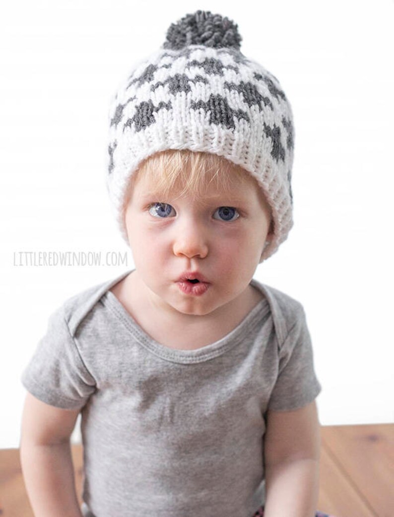 Puede incluir: Un ni&ntilde;o peque&ntilde;o con un gorro de punto gris y blanco con un pomp&oacute;n en la parte superior. El gorro tiene un patr&oacute;n geom&eacute;trico.