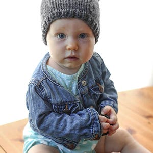 Baby looking at the camera surprised holding a lens cap and wearing a knit hat with bear ears on a wood table in front of a white background