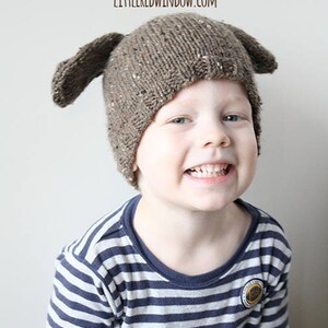 Puede incluir: Un ni&ntilde;o lleva un gorro de punto marr&oacute;n con orejas ca&iacute;das con forma de perro. El gorro tiene un patr&oacute;n moteado. El ni&ntilde;o sonr&iacute;e y lleva una camisa a rayas azul y blanca.