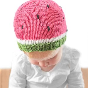 baby wearing a fun knit hat that looks like a watermelon slice complete with seeds looking down to the left
