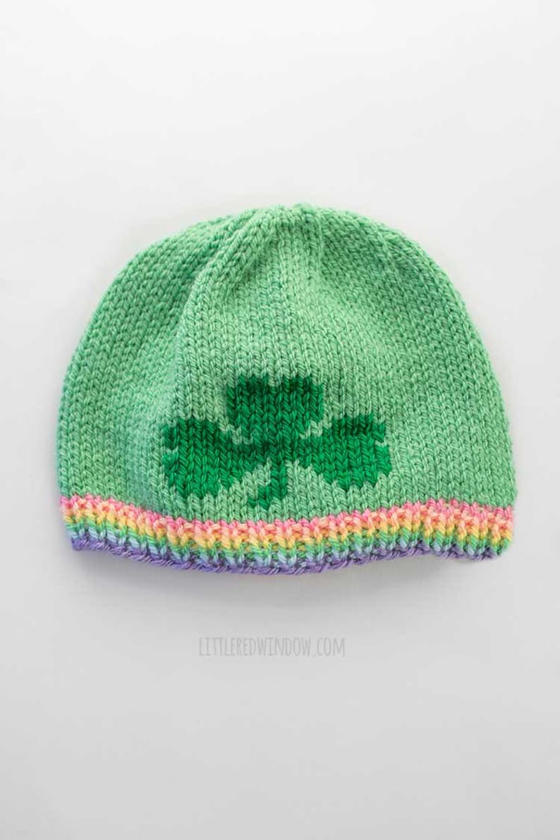 May include: Green knitted hat with a green shamrock design and a rainbow colored brim.