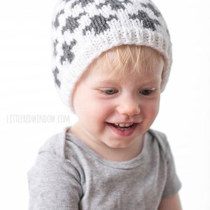 Puede incluir: Un ni&ntilde;o peque&ntilde;o con un gorro de punto gris y blanco con un pomp&oacute;n en la parte superior. El gorro tiene un patr&oacute;n geom&eacute;trico.