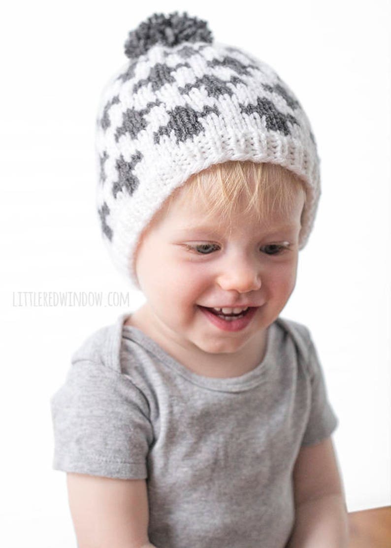 Puede incluir: Un ni&ntilde;o peque&ntilde;o con un gorro de punto gris y blanco con un pomp&oacute;n en la parte superior. El gorro tiene un patr&oacute;n geom&eacute;trico.