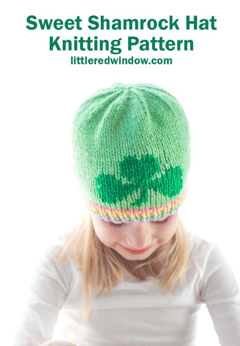 Child sporting a cozy green hat adorned with a shamrock design and a vibrant rainbow brim. Text above reads: "Sweet Shamrock Hat Knitting Pattern littleredwindow.com.