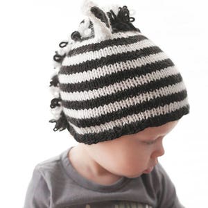 May include: A black and white striped knit hat with a white ear flap and a black and white striped brim. The hat is on a baby's head.