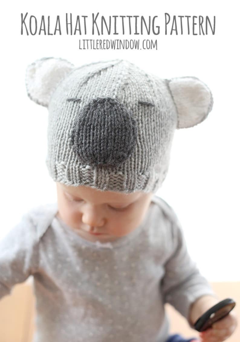 Chubby baby in a gray shirt wearing a gray knit hat that looks like a koala looking down at her lap