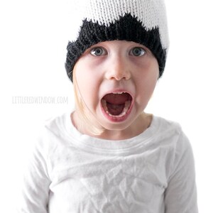 K&ouml;nnte beinhalten: Ein Kind tr&auml;gt eine wei&szlig;e und schwarze Strickm&uuml;tze mit einem l&auml;chelnden Gesicht. Die M&uuml;tze hat schwarze Augen und einen schwarzen Mund. Das Kind tr&auml;gt ein wei&szlig;es Hemd und hat den Mund in einem &uuml;berraschten Ausdruck ge&ouml;ffnet.