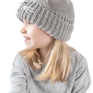 May include: A gray knitted beanie with a cat face embroidered on the front. The beanie is being worn by a child with long blonde hair.