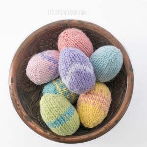 view from above of seven pastel colored knit Easter Eggs in various patterns in a dark brozne colored metal bowl on a white tabletop