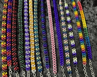 Könnte beinhalten: Eine Sammlung von 15 bunten Kettenhemdarmbändern mit silbernen Kettenverlängerungen. Die Armbänder sind aus verschiedenen farbigen Metallringen gefertigt und erzeugen so eine Vielzahl von Mustern.