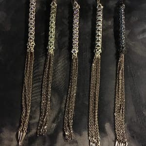 May include: Five silver chain whips with multiple strands and pointed tips. The chains are decorated with small, colorful beads.