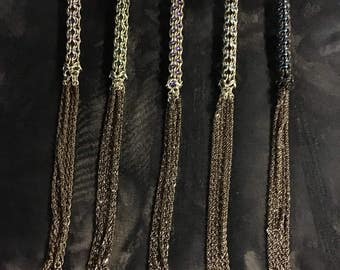 Könnte beinhalten: Fünf silberne Kettenpeitschen mit mehreren Strängen und spitzen Enden. Die Ketten sind mit kleinen, bunten Perlen verziert.