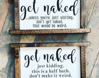 May include: Two rectangular wooden signs with white backgrounds and dark brown frames. The top sign reads "get naked" with additional text. The bottom sign also reads "get naked" with different text. The signs are designed for a bathroom.