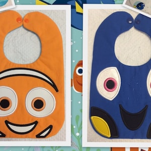 May include: Two baby bibs with embroidered characters from the movie Finding Nemo. One bib is orange with Marlin the clownfish and the other is blue with Dory the blue tang.
