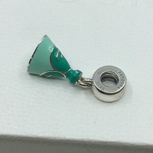 Puede incluir: Un charm de plata con un dise&ntilde;o de vestido en esmalte verde y azul. El charm tiene una cuenta redonda de plata con el texto "Pandora" y "ALE 925" en &eacute;l.