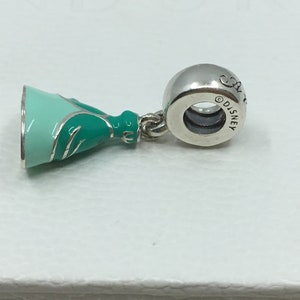 Puede incluir: Encanto de plata con un vestido de princesa verde y azul con ribete plateado. La parte posterior del encanto tiene la palabra "Disney" grabada.