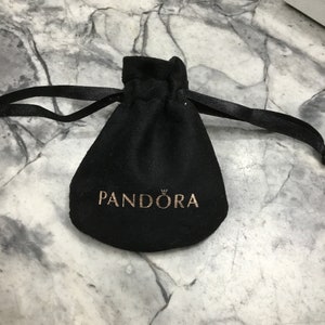 Puede incluir: Bolsa de terciopelo negro con cierre de cord&oacute;n y la palabra "PANDORA" impresa en letras doradas.