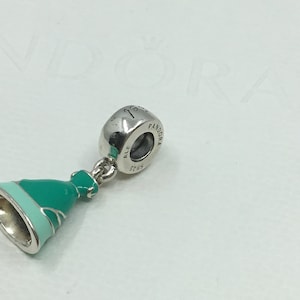 Puede incluir: Un charm de plata con un colgante de vestido de esmalte verde y azul. El charm est&aacute; marcado con "Pandora" y "ALE 5765".