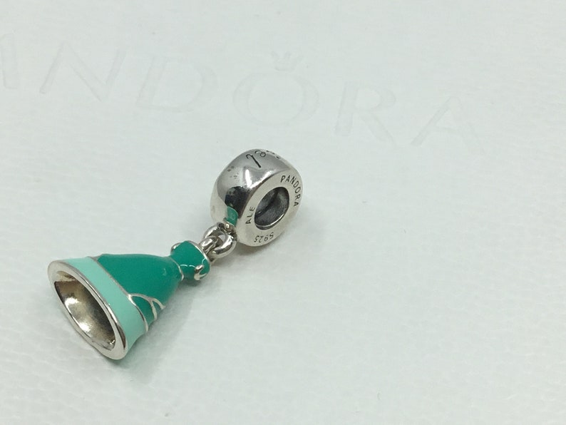 Puede incluir: Un charm de plata con un colgante de vestido de esmalte verde y azul. El charm est&aacute; marcado con "Pandora" y "ALE 5765".