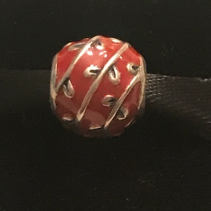 May include: A red and silver charm with a swirl design. The charm is round and has a shiny finish.
