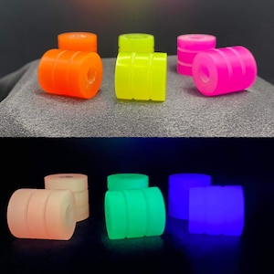 Puede incluir: Seis ruedas de monopatín que brillan en la oscuridad en diferentes colores: naranja, amarillo, rosa, verde, azul y blanco. Las ruedas están apiladas en pares.