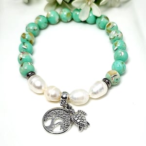 May include: A turquoise and white beaded bracelet with a silver charm of a tree and a turtle. The bracelet is made with small, round beads and has a pearl-like finish.