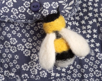 May include: A blue fabric pocket with a white floral pattern and a felt bee appliqué. The bee is yellow and black with white wings.