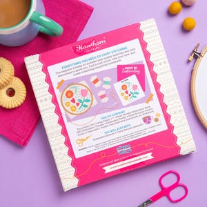 a sewing kit with various sewing tools and decorative elements, such as a teapot, cookies, and a pair of scissors, all set against a purple background.