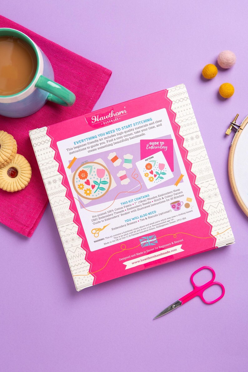 a sewing kit with various sewing tools and decorative elements, such as a teapot, cookies, and a pair of scissors, all set against a purple background.