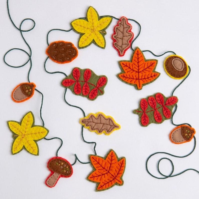 May include: A felt garland with autumn leaves and acorns in shades of yellow, orange, red, brown, and green. The garland is strung on a green twine.
