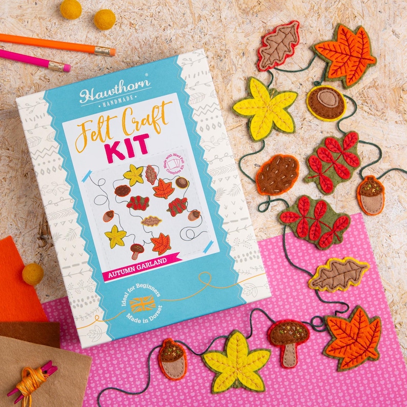 May include: A felt craft kit for making an autumn garland. The kit includes felt pieces in various fall colors, including orange, yellow, brown, and green, shaped like leaves, acorns, and pinecones. The kit also includes a length of twine for stringing the garland together. The box features the text "Felt Craft Kit" and "Autumn Garland".