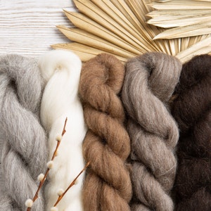 May include: Four skeins of yarn in different shades of brown, grey, and white. The yarn is arranged in a vertical row, with the white yarn in the centre.