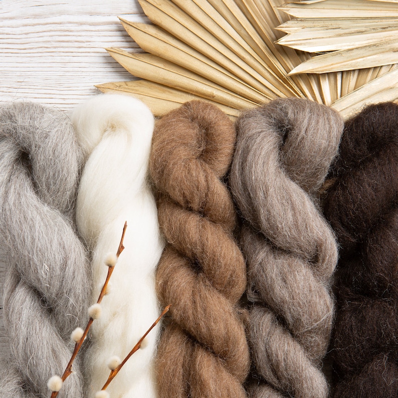May include: Four skeins of yarn in different shades of brown, gray, and white. The yarn is arranged in a vertical row, with the white yarn in the center.