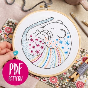 May include: A colorful embroidery pattern of a sleeping mouse with a rainbow tail and a starry body. The pattern is in a wooden embroidery hoop and is labeled "PDF PATTERN".