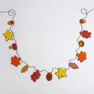 May include: A felt garland with autumn leaves, acorns, and mushrooms. The garland is strung on a green twine and is perfect for fall decor.