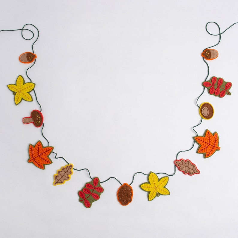 May include: A felt garland with autumn leaves, acorns, and mushrooms. The garland is strung on a green twine and is perfect for fall decor.