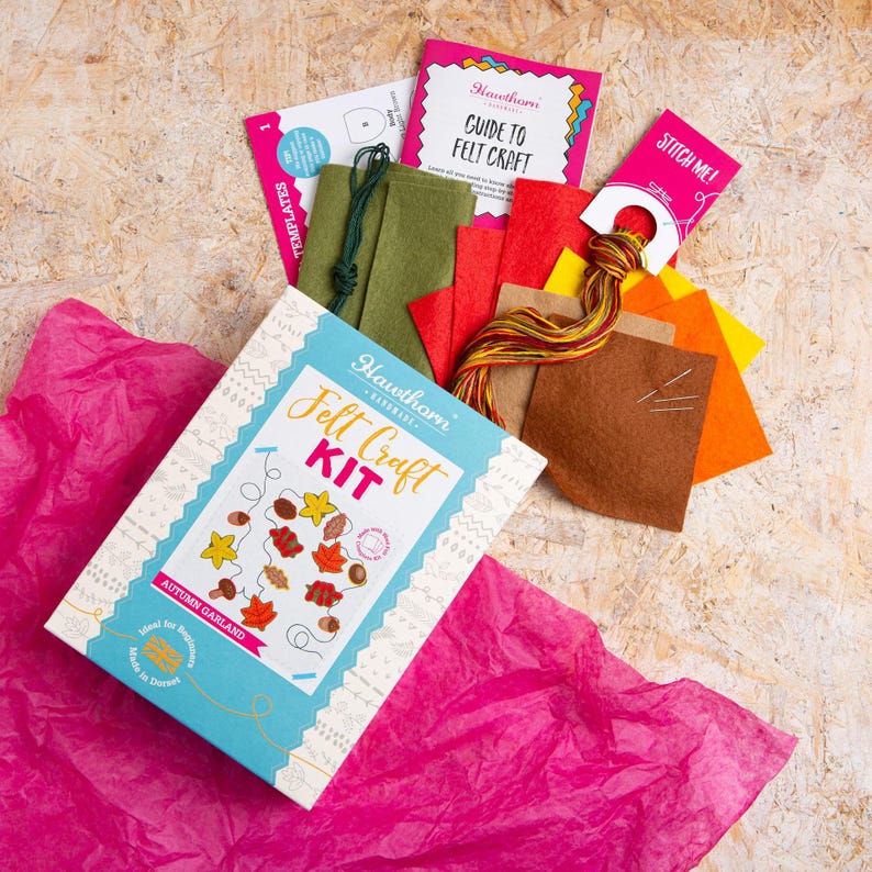 May include: A craft kit for making an autumn garland. The kit includes felt pieces in various fall colors, embroidery floss, needles, and a guide to felt craft. The box features a colorful illustration of the finished garland.