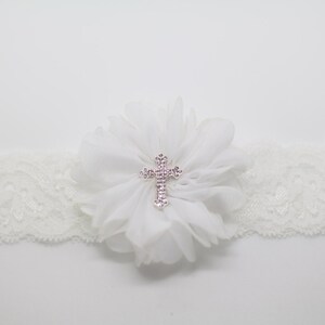 May include: Ivory lace garter with a white chiffon flower and a rhinestone cross centerpiece. The garter is a delicate accessory, perfect for special occasions.