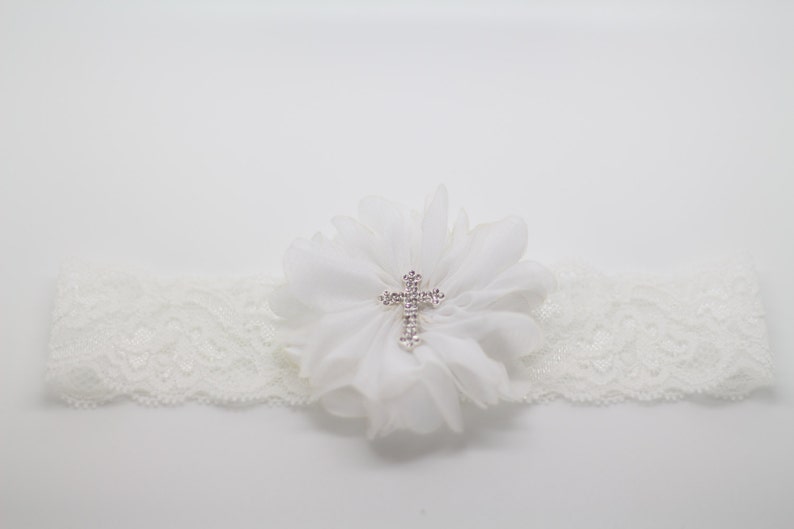 May include: Ivory lace garter with a white chiffon flower and a rhinestone cross. The garter is a delicate accessory, perfect for a wedding or special occasion. The lace band is approximately 1 inch wide.