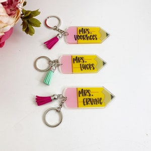 Puede incluir: Tres llaveros en forma de l&aacute;piz amarillo y rosa con borlas negras. Los llaveros tienen los nombres "Mrs. Voorhees", "Mrs. Lucks" y "Mrs. Ervine" escritos en ellos.