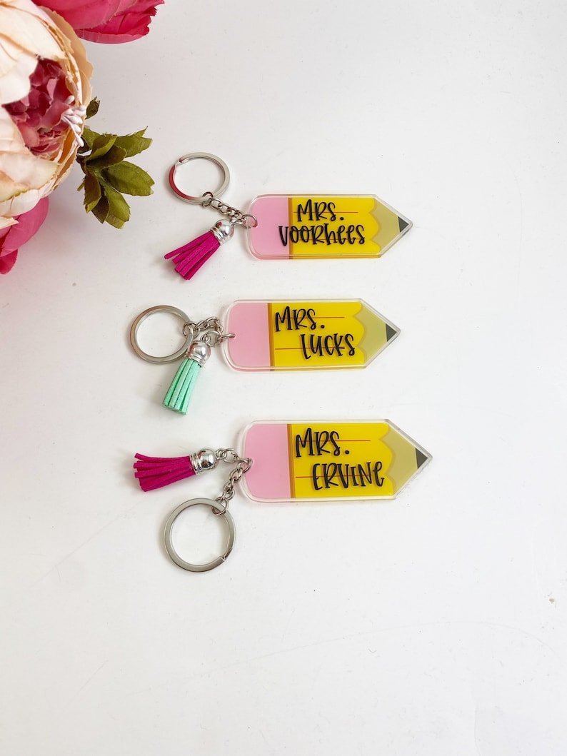 Puede incluir: Tres llaveros en forma de l&aacute;piz amarillo y rosa con borlas negras. Los llaveros tienen los nombres "Mrs. Voorhees", "Mrs. Lucks" y "Mrs. Ervine" escritos en ellos.