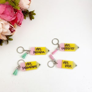 Puede incluir: Cuatro llaveros de acr&iacute;lico en forma de l&aacute;piz rosa y amarillo con borlas. Los llaveros est&aacute;n personalizados con los nombres "Mrs. Zaccari", "Mrs. Carpenter", "Mrs. Sabharwal" y "Mrs. Rosol".