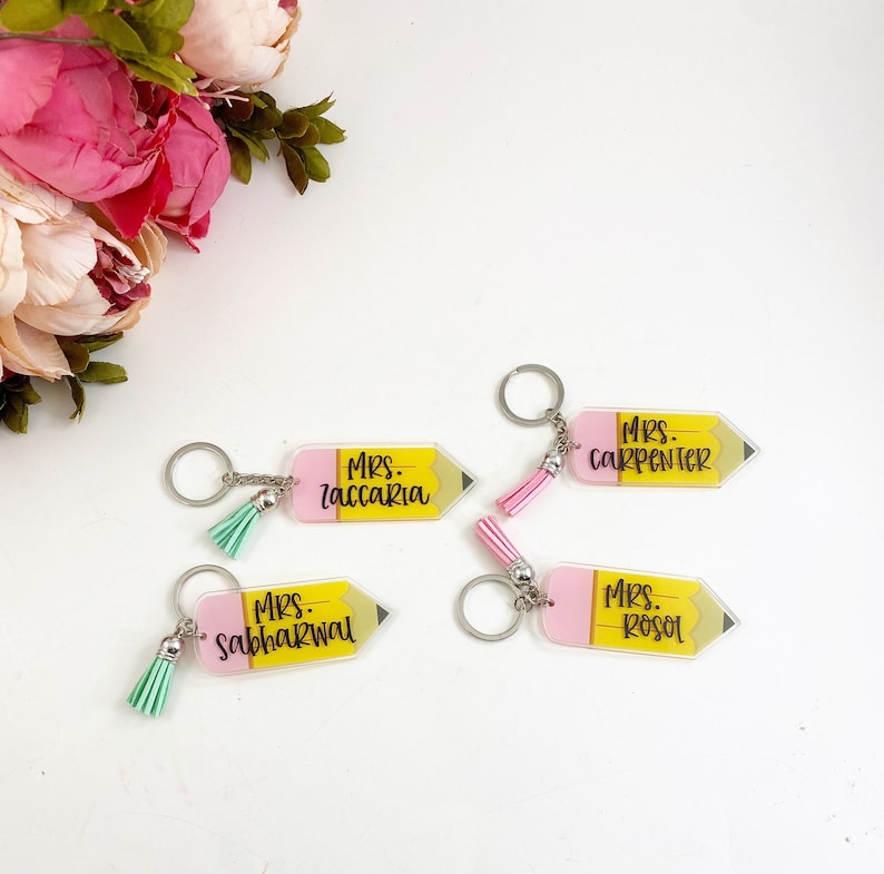 Puede incluir: Cuatro llaveros de acr&iacute;lico en forma de l&aacute;piz rosa y amarillo con borlas. Los llaveros est&aacute;n personalizados con los nombres "Mrs. Zaccari", "Mrs. Carpenter", "Mrs. Sabharwal" y "Mrs. Rosol".