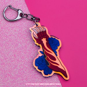 May include: A red and gold claw with blue roses, printed on a clear acrylic keychain. The keychain has a silver metal ring.