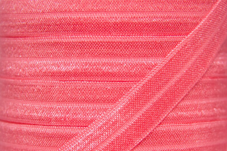 May include: Close-up of a spool of pink elastic ribbon. The ribbon is folded and has a shiny, satin-like finish.