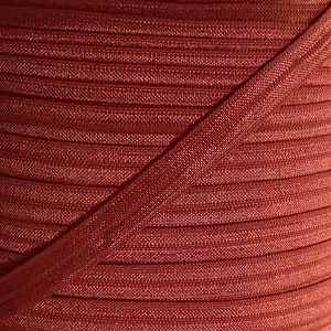 May include: Close-up of a roll of rust-colored ribbed elastic. The elastic is folded in half, showing the ribbed texture.