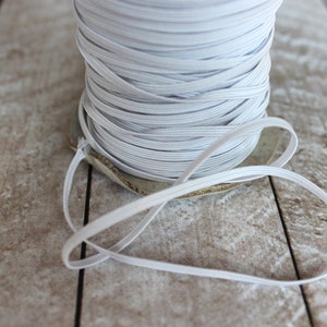 May include: A spool of white elastic cord, wound tightly and ready to be used for crafting projects.